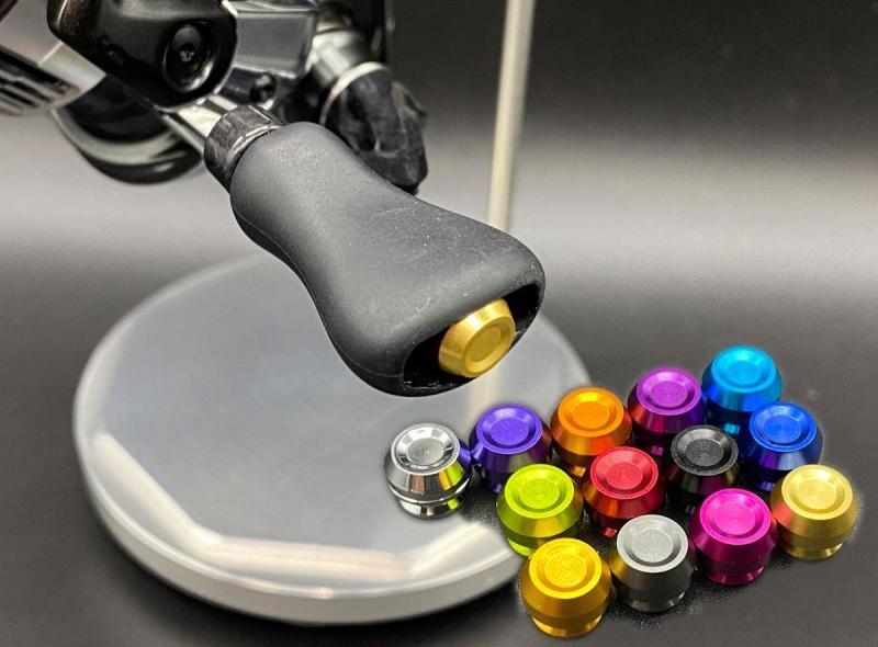 Eine Nahaufnahme der Hedgehog Studio Knob Cap für Shimano 23 Vanquish, 22 Aldebaran BFS und 23 Calcutta Conquest BFS mit goldenem Akzent. Daneben sind zwölf bunte Metallkappen abgebildet – ein ideales Upgrade für Ihre Shimano-Rolle.