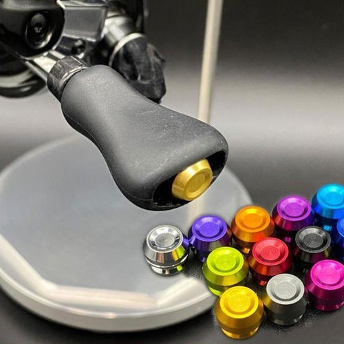 Eine Nahaufnahme der Hedgehog Studio Knob Cap für Shimano 23 Vanquish, 22 Aldebaran BFS und 23 Calcutta Conquest BFS mit goldenem Akzent. Daneben sind zwölf bunte Metallkappen abgebildet – ein ideales Upgrade für Ihre Shimano-Rolle.