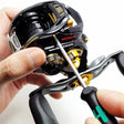 Eine Person justiert die schwarz-goldene Baitcaster-Rolle mit einem Schraubendreher einhändig und führt dabei eine Wartung mit dem Einbauservice Dragclicker von RL-Angelrollentuning durch.