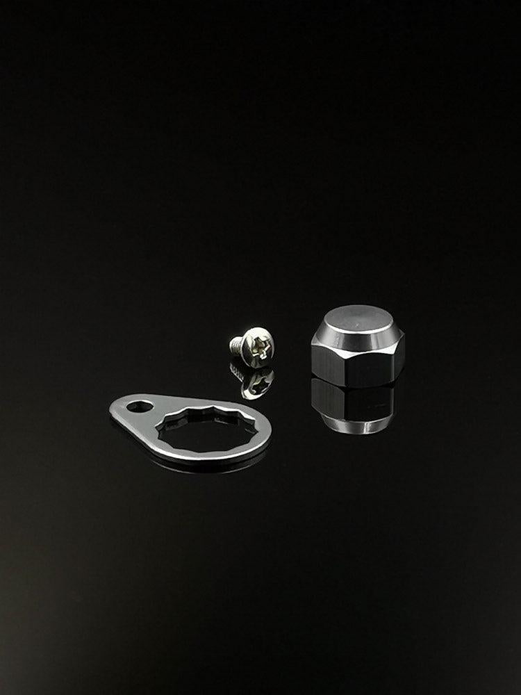 Eine RL-Angelrollentuning Kontermutter inkl. Plättchen M7 in Silber, samt flacher Metallplatte und Sechskant-Kontermutter, werden auf einer reflektierenden schwarzen Fläche dargestellt.