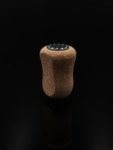 Der RL-TNG Kork Knob 20mm von RL-Angelrollentuning – ein einzelner Korkgriff mit schwarzer Folienoberfläche – steht aufrecht vor einem schwarzen Hintergrund und erzeugt eine subtile Reflexion darunter. Universelle Passform für vielseitigen Einsatz.