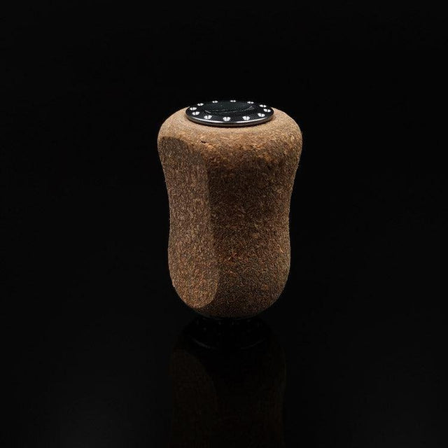 Der RL-TNG Kork Knob 20mm von RL-Angelrollentuning – ein einzelner Korkgriff mit schwarzer Folienoberfläche – steht aufrecht vor einem schwarzen Hintergrund und erzeugt eine subtile Reflexion darunter. Universelle Passform für vielseitigen Einsatz.