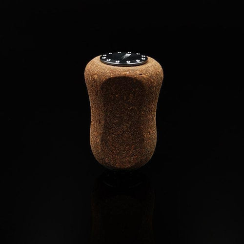 Ein einzelner RL-TNG Kork Knob 20 mm | Griff | Universal Fit von RL-Angelrollentuning mit dunkler Oberseite und Drahtmarkierungen steht aufrecht auf einer glatten schwarzen Oberfläche vor einem schlichten schwarzen Hintergrund.