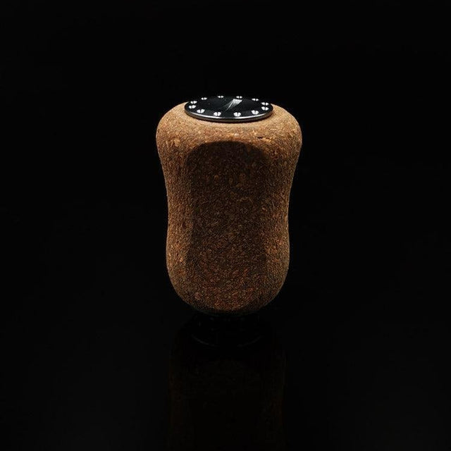 Ein einzelner RL-TNG Kork Knob 20 mm | Griff | Universal Fit von RL-Angelrollentuning mit dunkler Oberseite und Drahtmarkierungen steht aufrecht auf einer glatten schwarzen Oberfläche vor einem schlichten schwarzen Hintergrund.