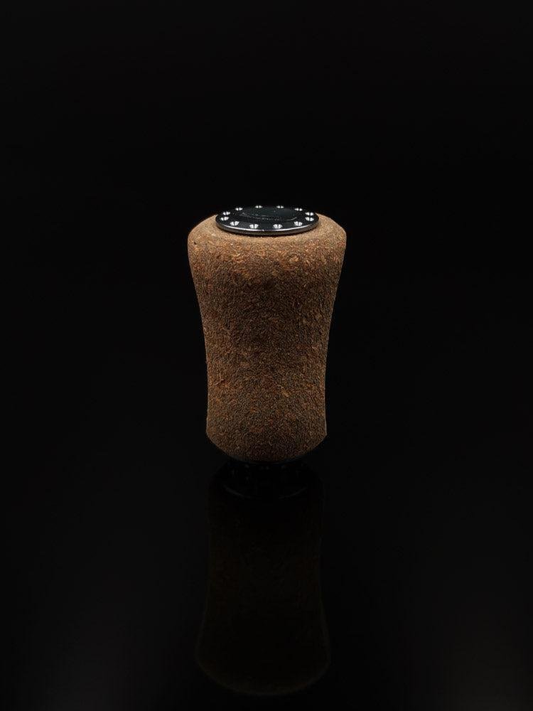 Ein einzelner RL-Angelrollentuning RL-TNG Kork-Knopf 20 mm | Griff | Universal Fit mit einer schwarz-weißen runden Oberseite steht aufrecht vor einem soliden schwarzen Hintergrund und erinnert an Details hochwertiger Angelmechanismen.