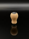 Der RL-TNG Kork Knob 20mm | Erdnuss | Universal Fit von RL-Angelrollentuning steht aufrecht auf einer reflektierenden schwarzen Oberfläche, sein abgerundeter Korkstopfen und die schwarze runde Basis spiegeln sich darunter.