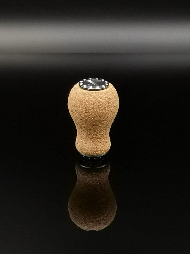 Der RL-TNG Kork Knob 20mm | Erdnuss | Universal Fit von RL-Angelrollentuning steht aufrecht auf einer reflektierenden schwarzen Oberfläche, sein abgerundeter Korkstopfen und die schwarze runde Basis spiegeln sich darunter.