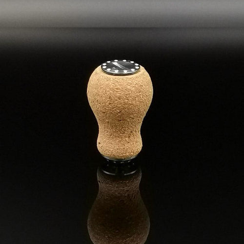 Der RL-TNG Kork Knob 20mm | Erdnuss | Universal Fit von RL-Angelrollentuning steht aufrecht auf einer reflektierenden schwarzen Oberfläche, sein abgerundeter Korkstopfen und die schwarze runde Basis spiegeln sich darunter.