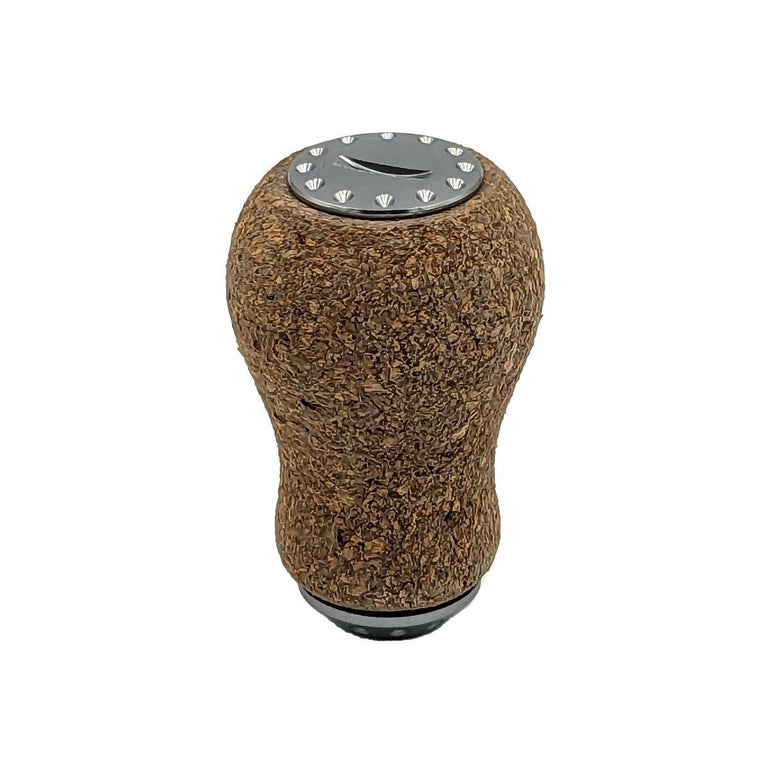 Der RL-Angelrollentuning RL-TNG Korkknopf 20 mm „Peanut“ Universal Fit verfügt über eine abgerundete Korkabdeckung, eine metallische Oberseite mit Schichtmuster und dekorative Nieten, inspiriert von Edelstahlkugellagern, isoliert auf Weiß dargestellt.