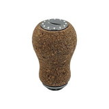 Der RL-Angelrollentuning RL-TNG Korkknopf 20 mm „Peanut“ Universal Fit verfügt über eine abgerundete Korkabdeckung, eine metallische Oberseite mit Schichtmuster und dekorative Nieten, inspiriert von Edelstahlkugellagern, isoliert auf Weiß dargestellt.