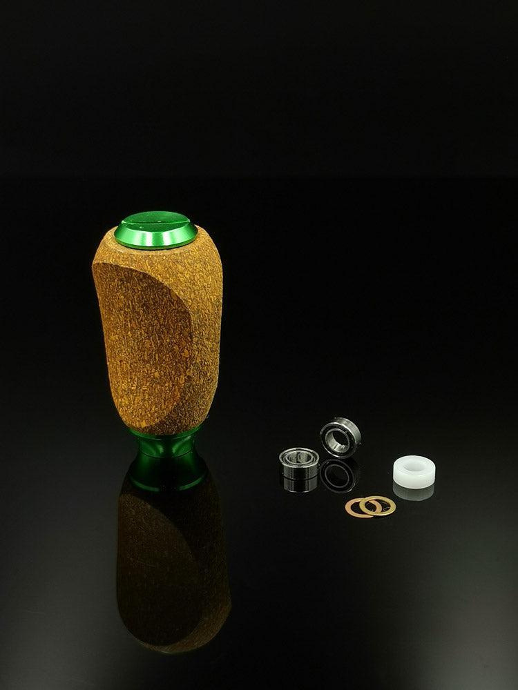 Ein RL-TNG Kork Knob von RL-Angelrollentuning mit strukturiertem Mehrfarbendesign steht aufrecht auf einer schwarzen Oberfläche, neben kleinen Metall- und Kunststoffteilen wie Lagern, Unterlegscheiben und einer zylindrischen Angelrollenkomponente.