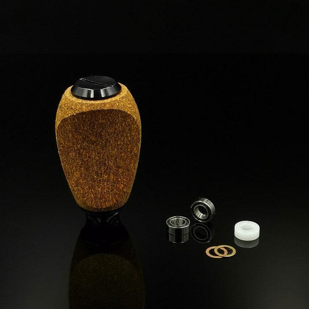 Der RL-TNG Kork Knob von RL-Angelrollentuning, ein strukturierter ovaler Knopf mit universeller Passform in mehreren Farben, steht aufrecht auf einer schwarzen Oberfläche neben Lagern, Unterlegscheiben und einem weißen Kunststoffring.