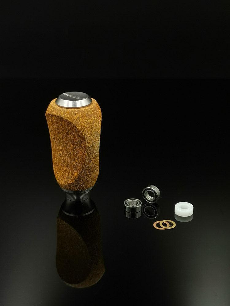 Der RL-TNG Kork Knob von RL-Angelrollentuning, ein mehrfarbiger ergonomischer Griff mit universeller Passform, steht aufrecht auf einer schwarzen reflektierenden Oberfläche neben ordentlich angeordneten demontierten Lagern, Unterlegscheiben und einem weißen Kunststoffring für eine Angelrolle.