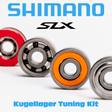 Eine Nahaufnahme von vier bunten Kugellagern mit dem Text „RL-TNG Kugellager Tuning Kit für Shimano SLX, SLX DC & SLX MGL – Spulenlager & Pinionlager Upgrade“ von RL-Angelrollentuning in Blau und Schwarz oben und unten auf weißem Hintergrund.