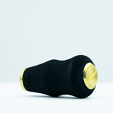 Der RL-TNG OCT 24 EVA-Knopf von RL-TNG, ein schwarzer Kurbelknauf mit goldenen Endkappen, besteht aus EVA-Material für besseren Halt. Er hat eine strukturierte Oberfläche und eine schlichte zylindrische Form, die auf einer weißen Oberfläche vor hellem Hintergrund dargestellt ist.