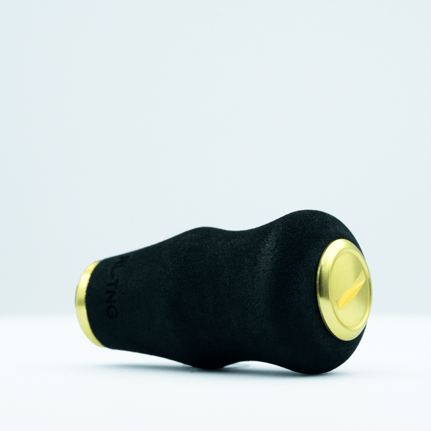Der RL-TNG OCT 24 EVA-Knopf von RL-TNG, ein schwarzer Kurbelknauf mit goldenen Endkappen, besteht aus EVA-Material für besseren Halt. Er hat eine strukturierte Oberfläche und eine schlichte zylindrische Form, die auf einer weißen Oberfläche vor hellem Hintergrund dargestellt ist.