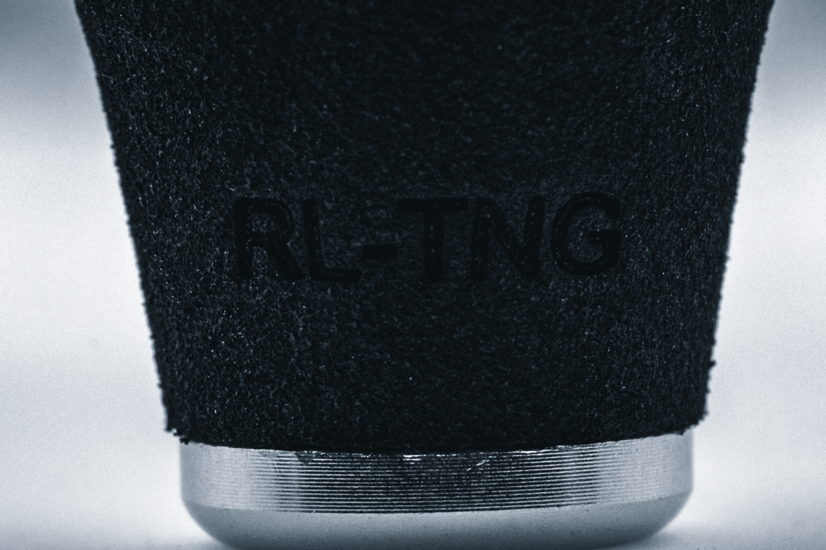 Nahaufnahme des RL-TNG OCT 24 EVA-Knopfes von RL-TNG mit strukturierter schwarzer Oberfläche, eingraviertem Branding und einem metallisch-silbernen Band an der Unterseite. Hergestellt aus EVA-Material für maximalen Halt, vor neutralem Hintergrund.