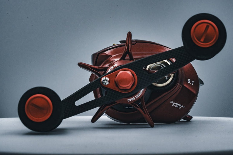 Eine Nahaufnahme der Angelrolle RL-TNG OCT 24 EVA Knob von RL-TNG mit rotem Gehäuse, orangefarbenen Akzenten und schwarzem EVA-Knob-Griff, dargestellt auf einer hellen Oberfläche mit sichtbarem Markenzeichen und mechanischen Details vor grauem Hintergrund.