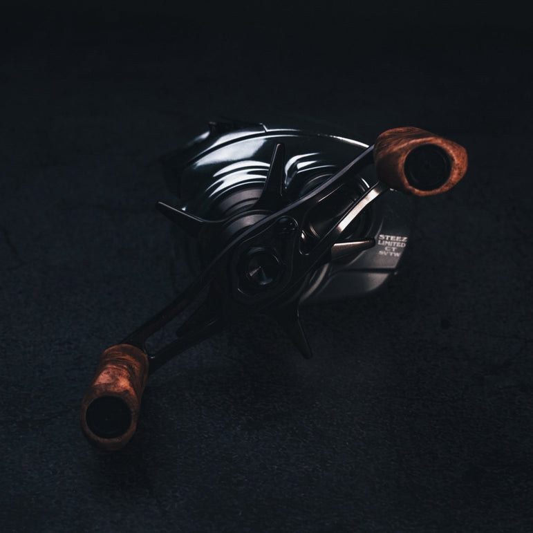 Nahaufnahme vom SLP Works i Shape Wood Knob Limited Edition – perfekt fürs Reel-Tuning! Der stilvolle Holzknauf glänzt mit einzigartiger Maserung und coolen Metall-Details vor dunklem Hintergrund. Mit dem richtigen Licht werden die schicken Akzente richtig in Szene gesetzt. Wenn du deinem Angelsetup ein Upgrade verpassen willst, geht’s nicht edler!.