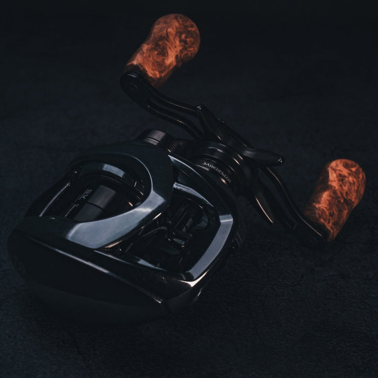 Nahaufnahme vom SLP Works i Shape Wood Knob Limited Edition – das schicke schwarze Baitcaster-Griffstück von SLP Works, perfekt zum Tunen deiner Angelrolle! Edler Holz-Knauf, frisches Design und mega Grip für extra Style am Wasser. Fotografiert vor dunklem Hintergrund, damit du jedes Detail siehst und direkt merkst: Damit hebst du dein Tackle auf’s nächste Level!.