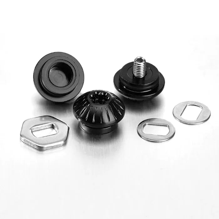 Drei schwarze Gomexus Aluminiummuttern (Schwarz) und zwei silberne Unterlegscheiben mit Kontermutter sind auf einer weißen Fläche angeordnet. Eine Mutter hat eine sichtbare Schraube, eine andere weist ein gezahntes Design auf.