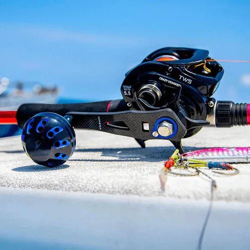 Nahaufnahme einer schwarzen Angelrolle mit dem Gomexus Carbon Handle 75 mm mit 38 mm Power Knob (8x5mm) von Gomexus, die an einer Angelrute befestigt ist, mit Angelködern und Haken auf einer weißen Fläche vor einem blauen Himmel im Hintergrund.