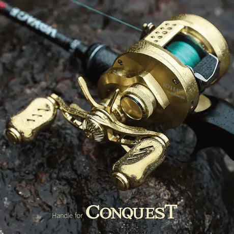 Ein 90-mm-Griff aus goldenem Aluminium von Gomexus mit 22-mm-Titanknöpfen (7 x 4 mm) ist an einer schwarzen Angelrolle und -rute auf einem nassen, dunklen Felsen befestigt. Stilvolle goldene Titanknöpfe fallen auf, darunter der Schriftzug „Handle for CONQUEST“.